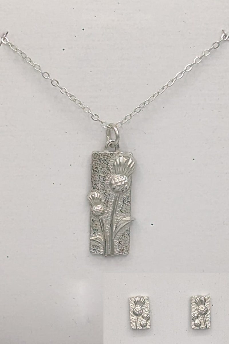 A silver necklace adorned with a rectangular pendant, complemented by a thistle design.